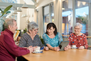 Neljä senioria istuu kahvipöydän ääressä, yhden kädessä on tabletti